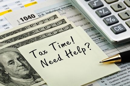 Tax form with note reading “Tax Time! Need Help?” beside calculator and pen