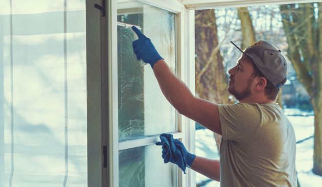 Worker in gloves washing a window outside a building, reaching up with a squeegee