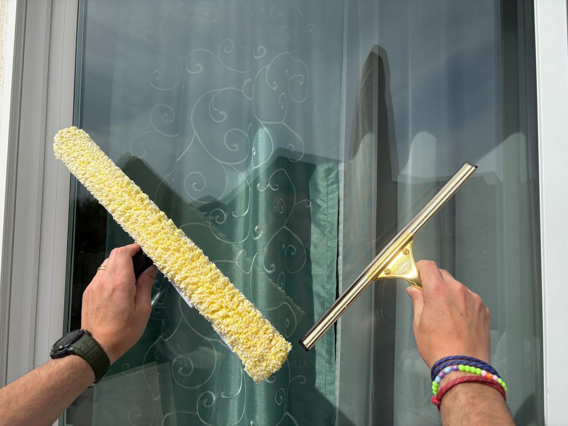 Hands holding a yellow roller and a squeegee against a glass window
