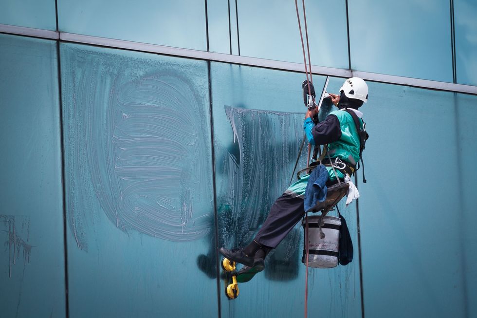 Window cleaner suspended on ropes cleaning a large blue glass building facade