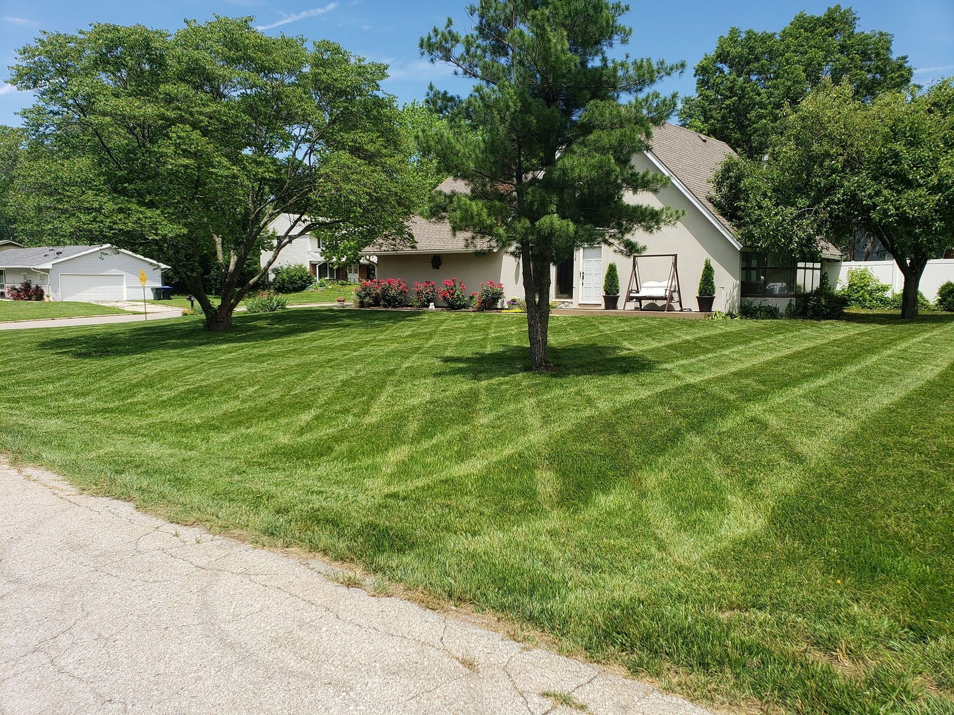 Lawn mowed with striped patterns in front of a house, golf cart, and trees on a sunny day.