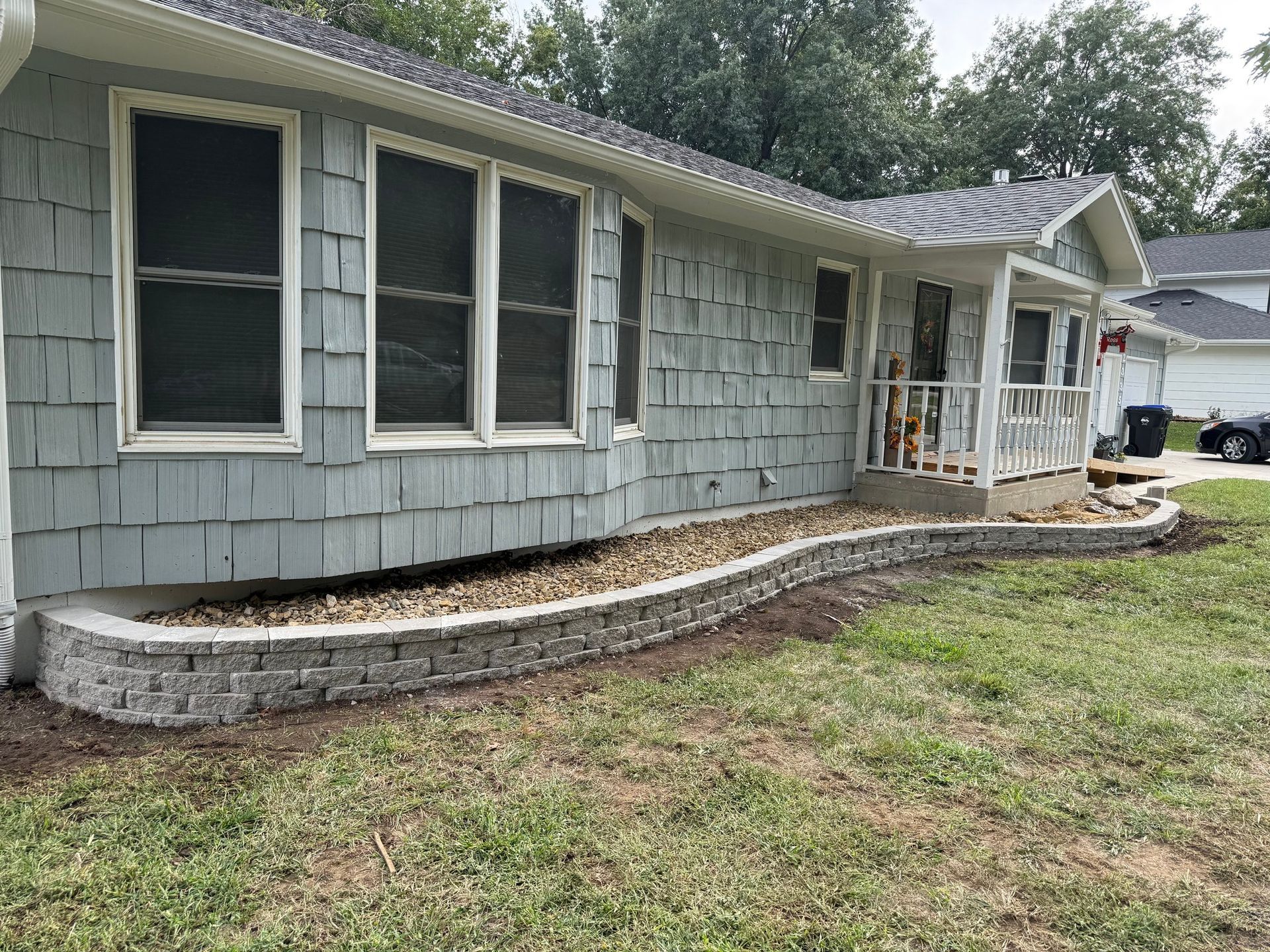 Gray house with blue-gray shingles and a small stone retaining wall along the front yard.