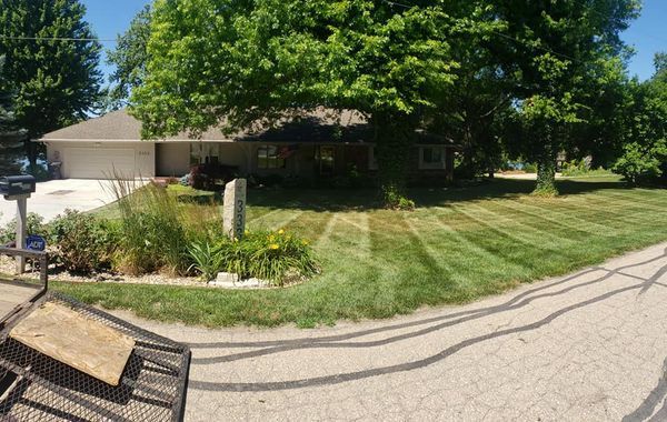 House with a green lawn and tree, striped from recent mowing, on a sunny day.