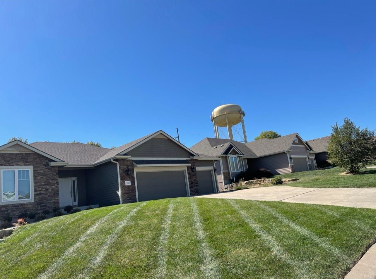 Row of houses with green lawns on a sunny day. A water tower is visible in the background.