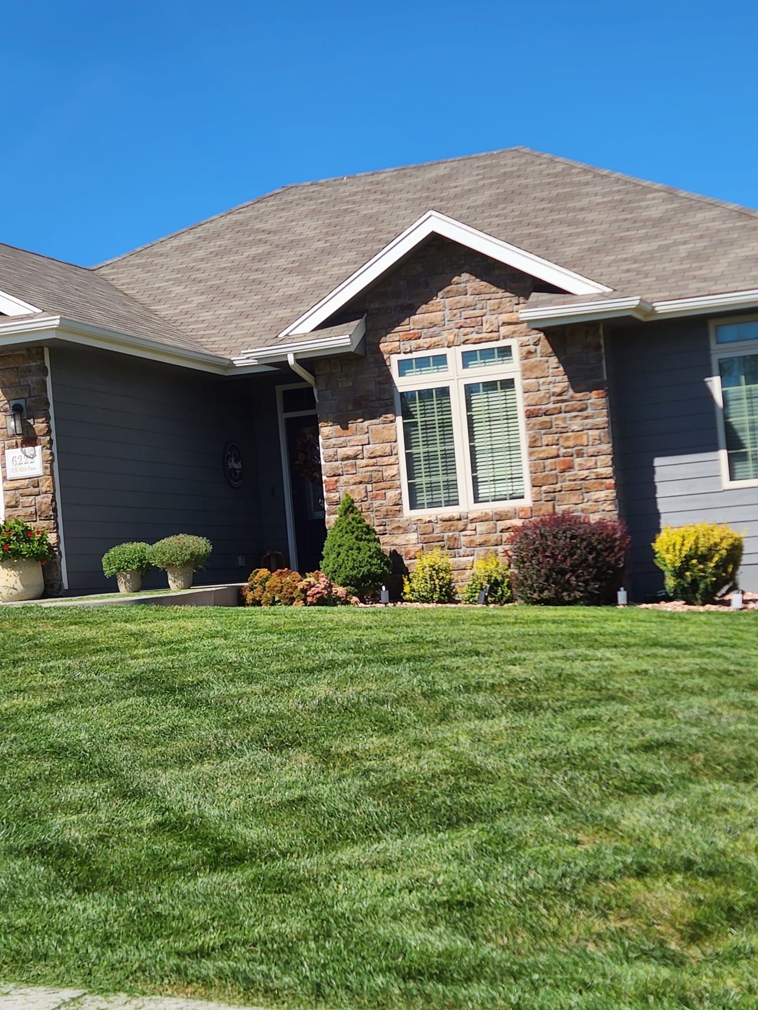 House with brick facade and gray siding, green lawn, blue sky.