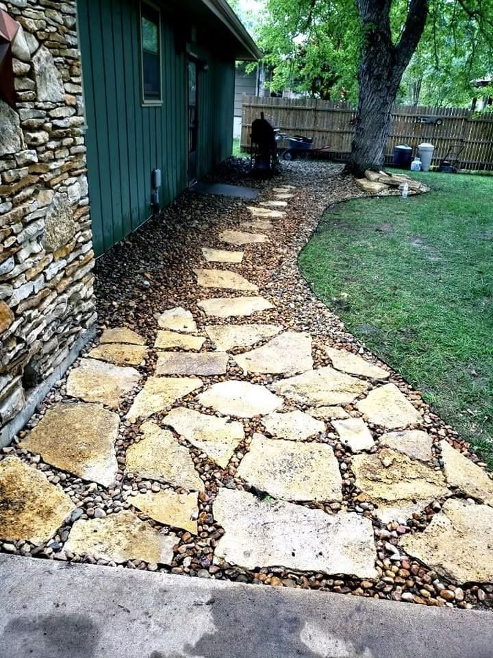 Flagstone pathway with gravel edging next to a green house and a stone wall.