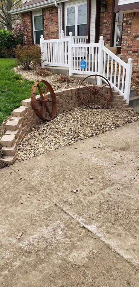 A home's front yard with brick retaining wall, gravel, and rusty wagon wheels as decor.