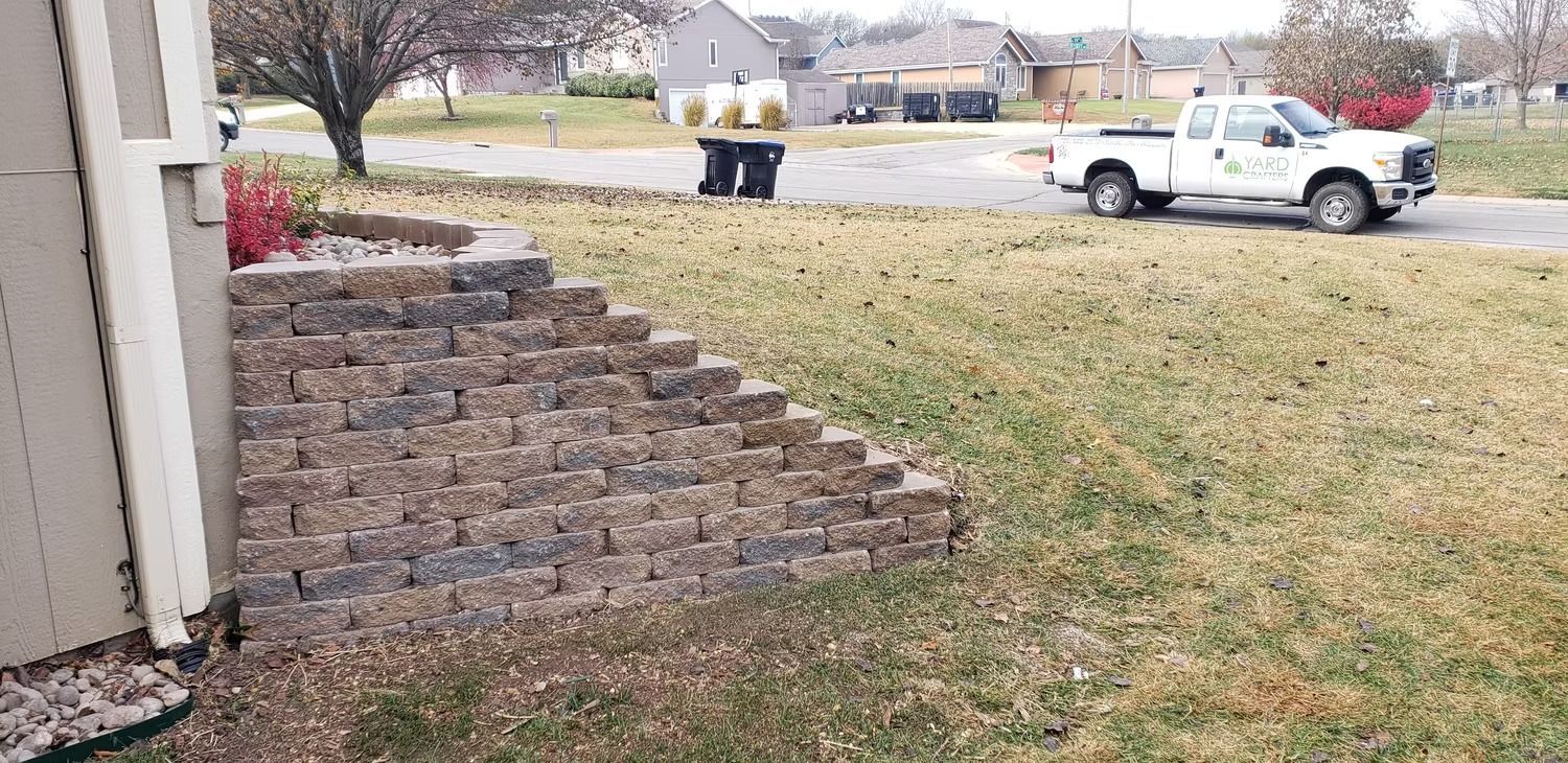 A white pickup truck parked in front of a house. In the foreground is a brick retaining wall and lawn.
