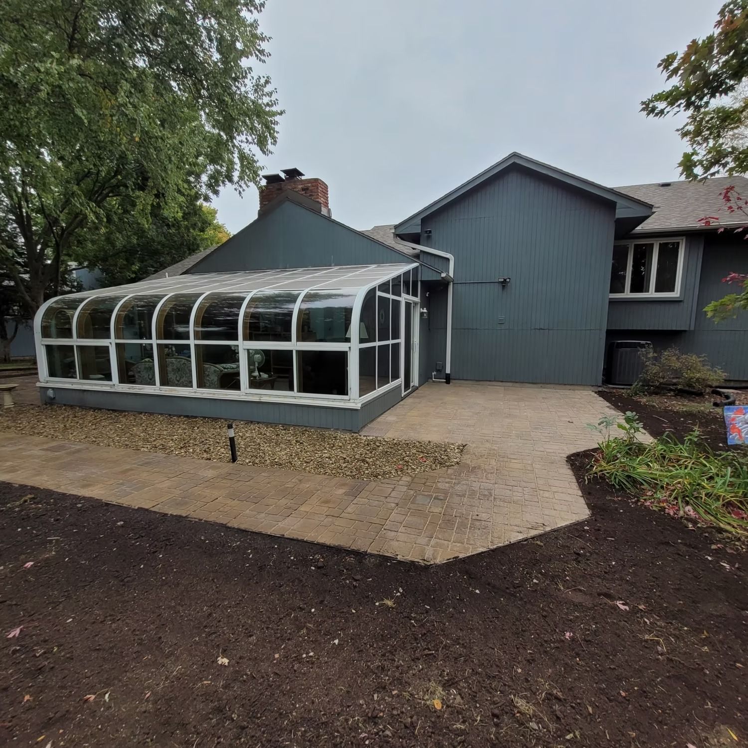 A house with a sunroom, patio, and freshly tilled dirt in the yard.