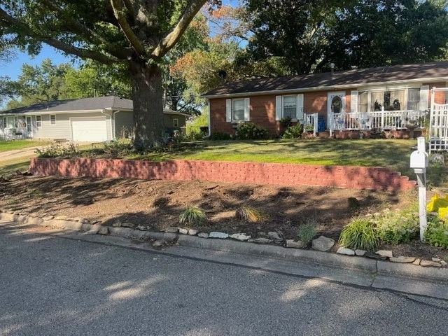 Low brick retaining wall with landscaping bed in front of a red brick house and lawn.