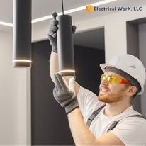 A man wearing a hard hat and safety glasses is installing a light fixture.