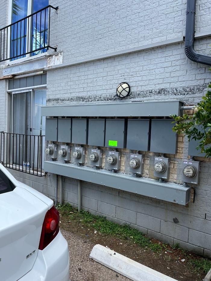 A white car is parked in front of a building with a bunch of electrical boxes on it.