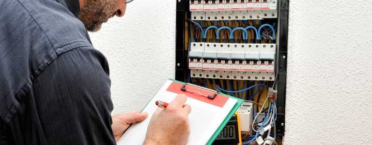 A man is writing on a clipboard in front of an electrical box.