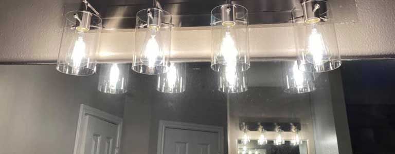 A bathroom mirror with a chandelier hanging from it.