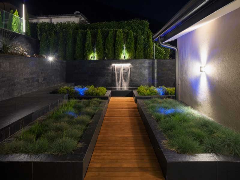 A wooden walkway leading to a waterfall in a garden at night.