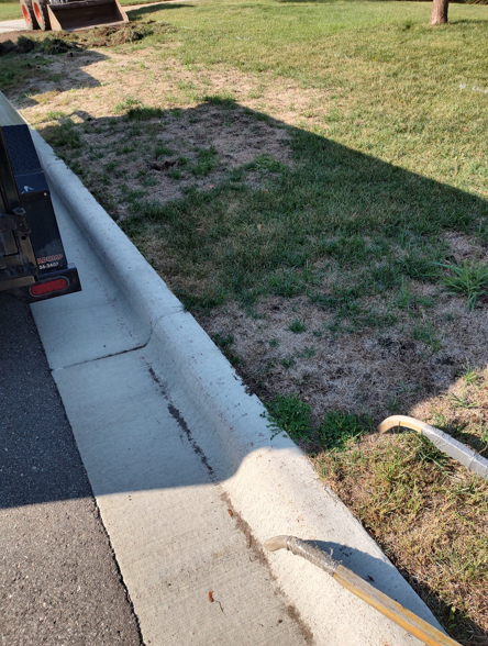 A concrete curb alongside a street edge and a patch of dry grass and dirt.