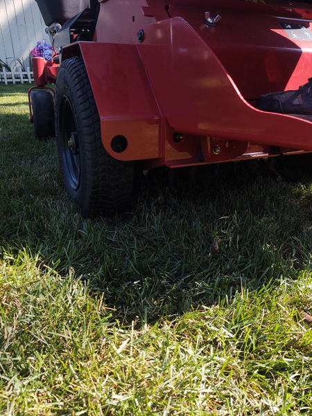 A low-angle view of the rear wheel and red frame of a riding lawn mower parked on green grass.