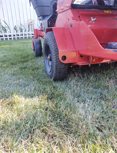 A low-angle view of the rear tire and red metal frame of a commercial lawn mower parked on a residential lawn.