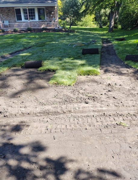 A residential yard in the process of being resodded, showing patches of new grass rolls laid out on prepared dark soil.