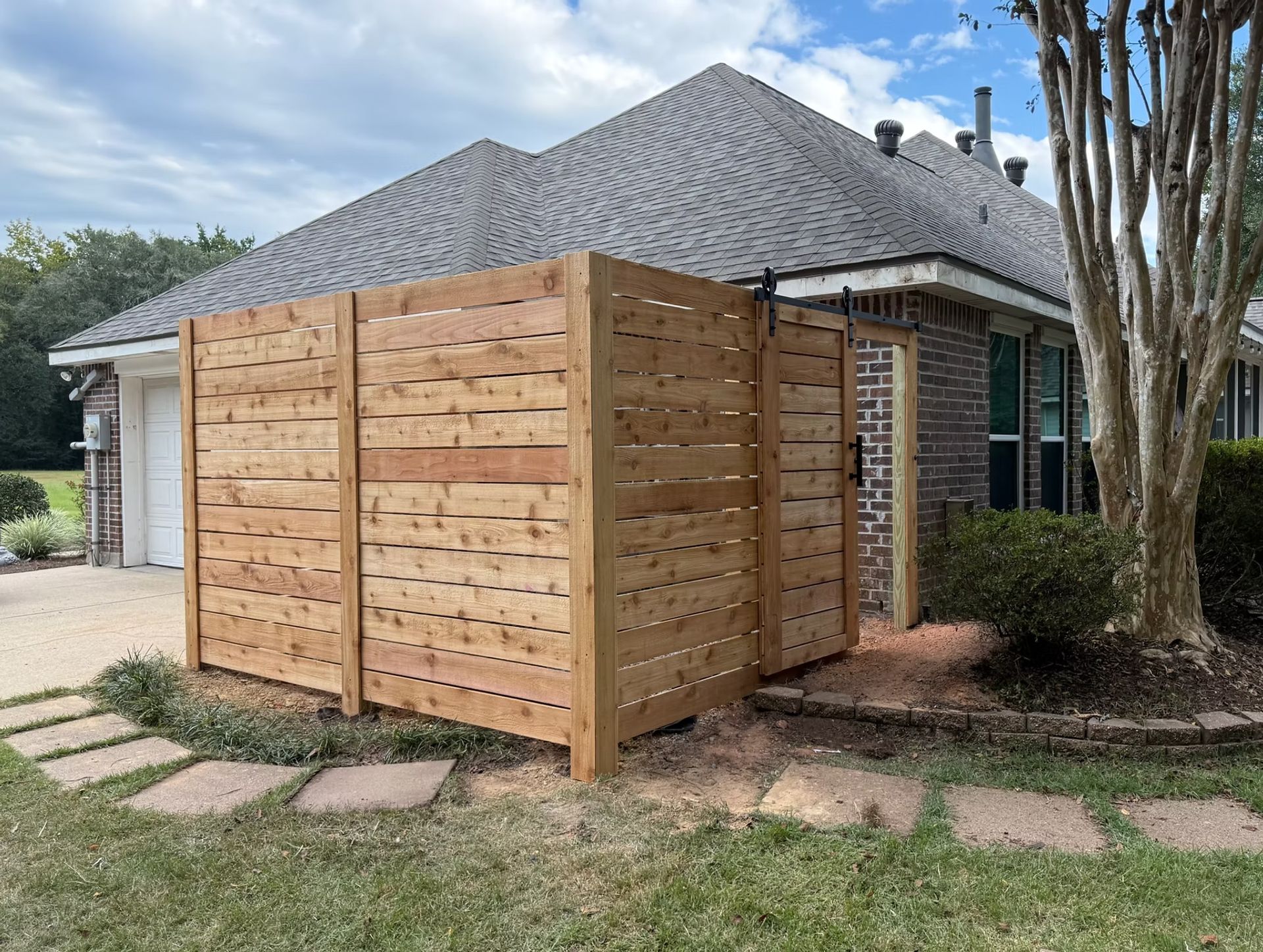 Wooden privacy fence next to a house with a gray roof and stepping stones in the yard.