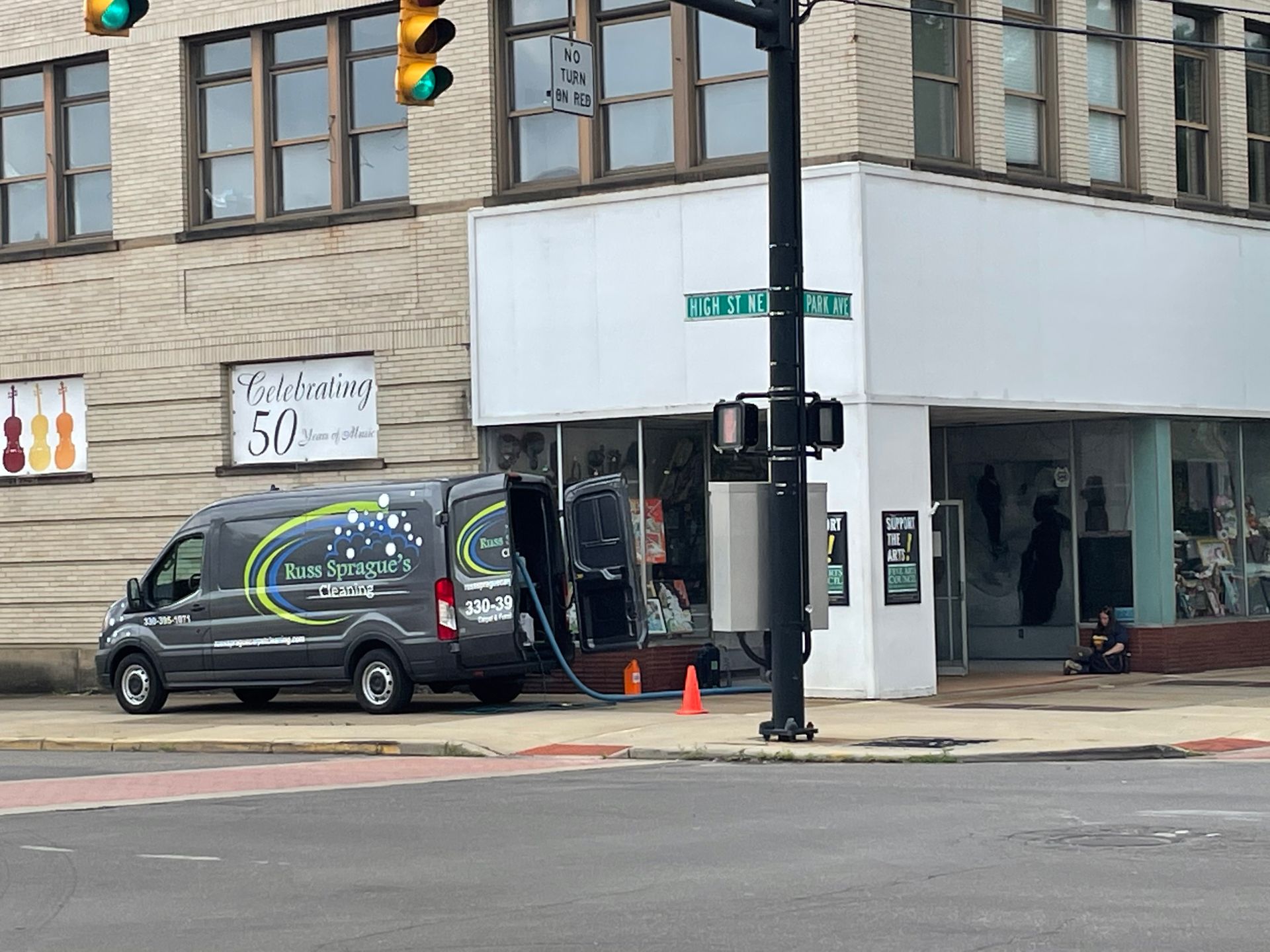 Black van parked at a city storefront with orange cones and traffic lights at the corner.