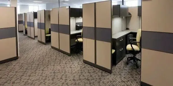 Office cubicles in a carpeted workspace, with beige-and-gray partitions and empty desks.