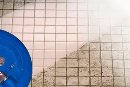 Dirty tiled floor with a blue bucket at the left edge