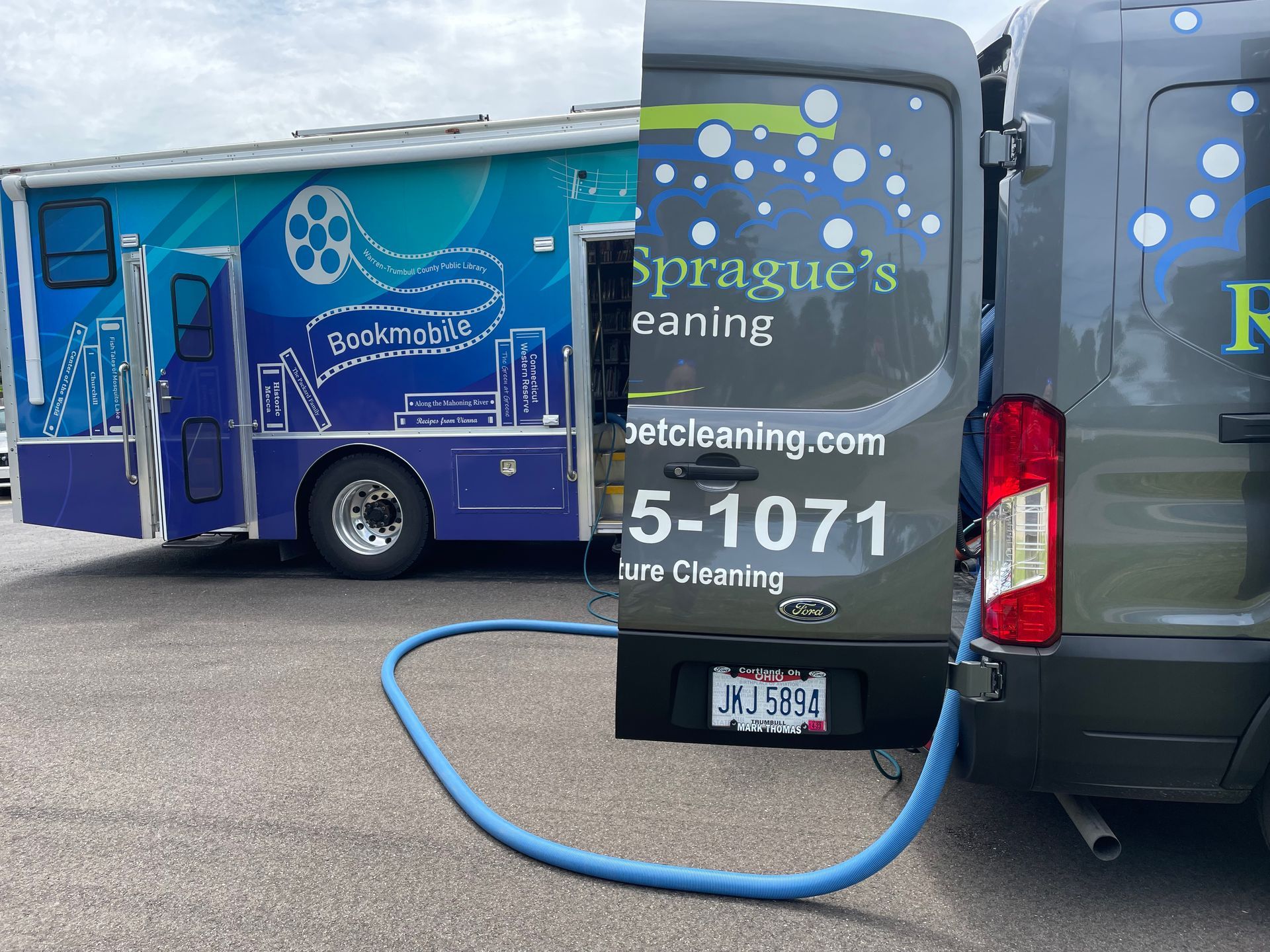 Two cleaning service vans parked side by side, with a blue hose connected between them.