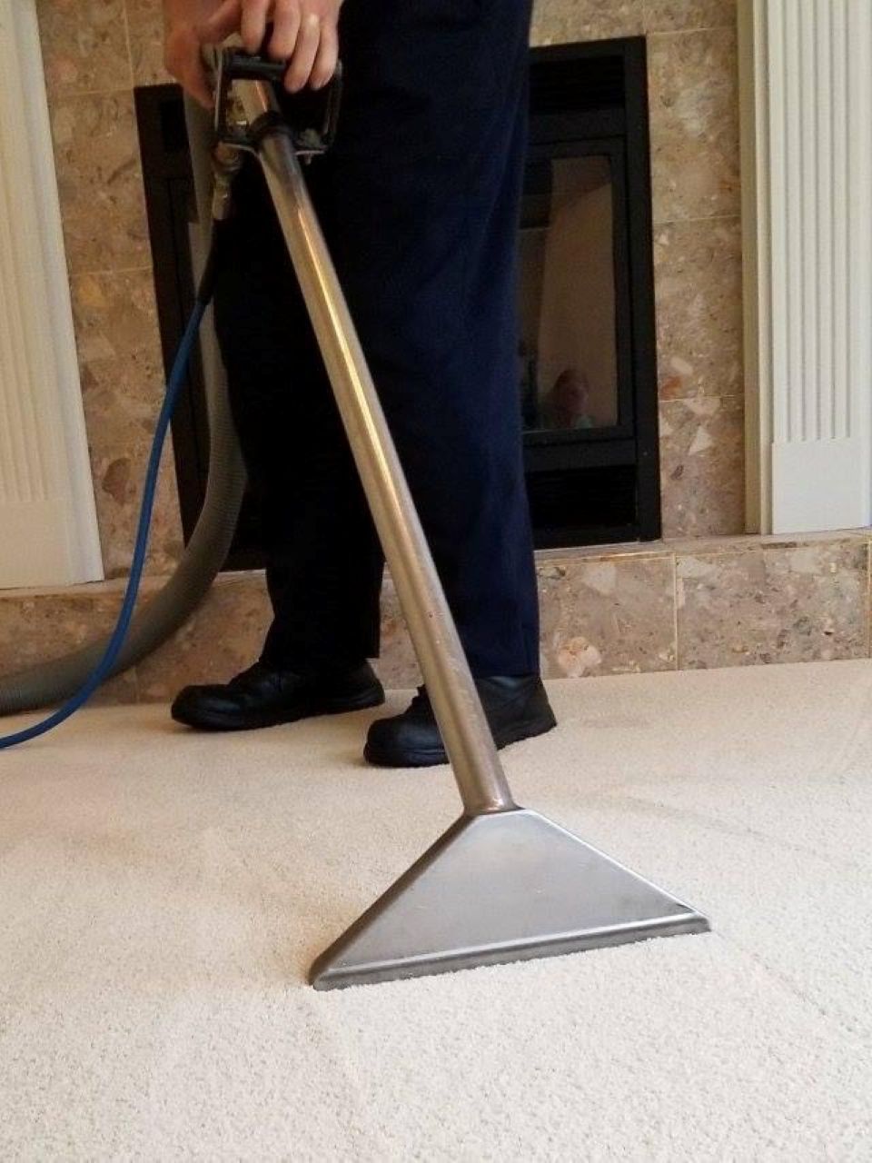 Carpet cleaning wand in use on a light beige carpet near a fireplace