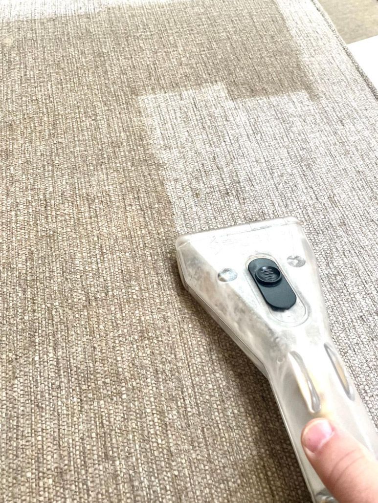 Hand using a carpet-cleaning tool on a beige patterned carpet.