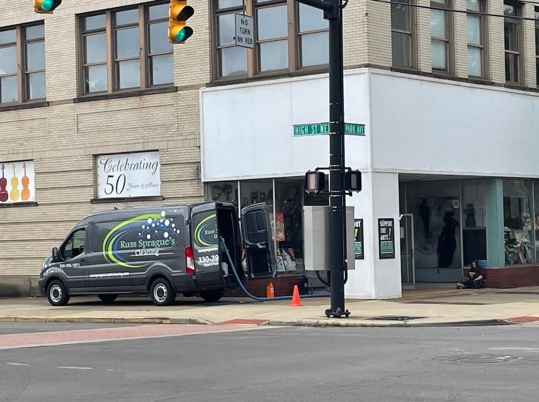 Black van parked at a street corner outside a storefront with a traffic light and orange cones