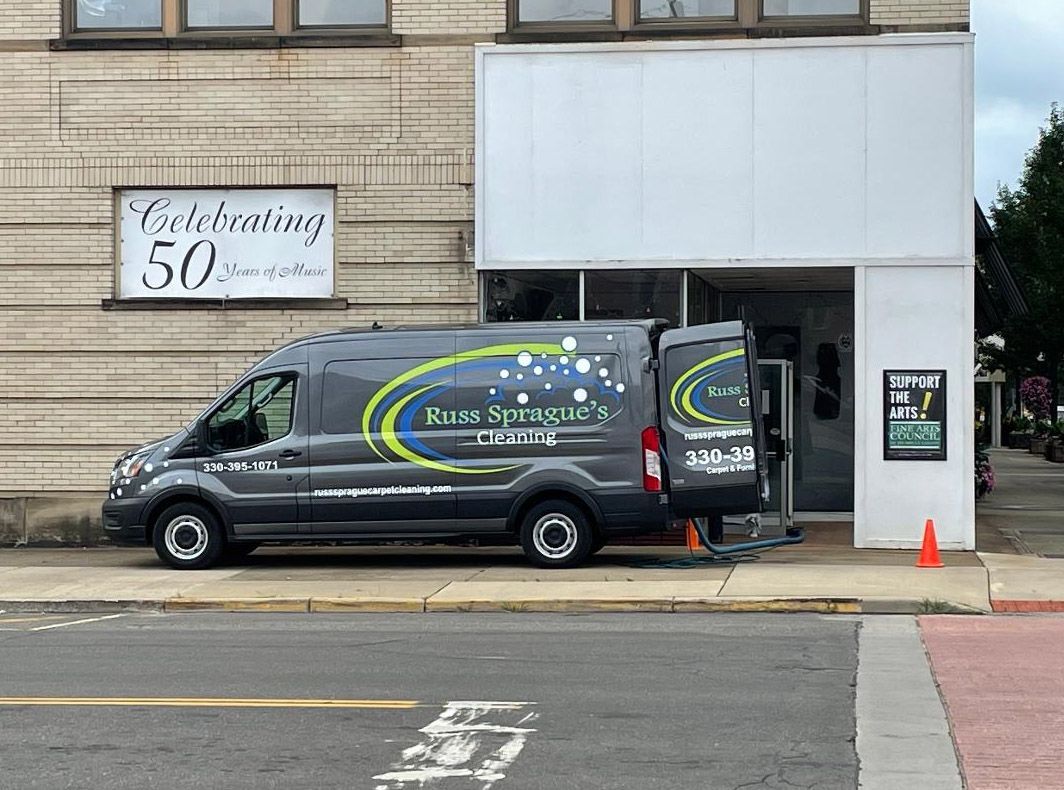 Black van with green logo parked beside a storefront entrance on a city street.