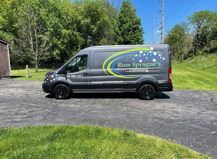 Black Russo Sprinter van parked on gravel by a grassy road with trees and a blue sky