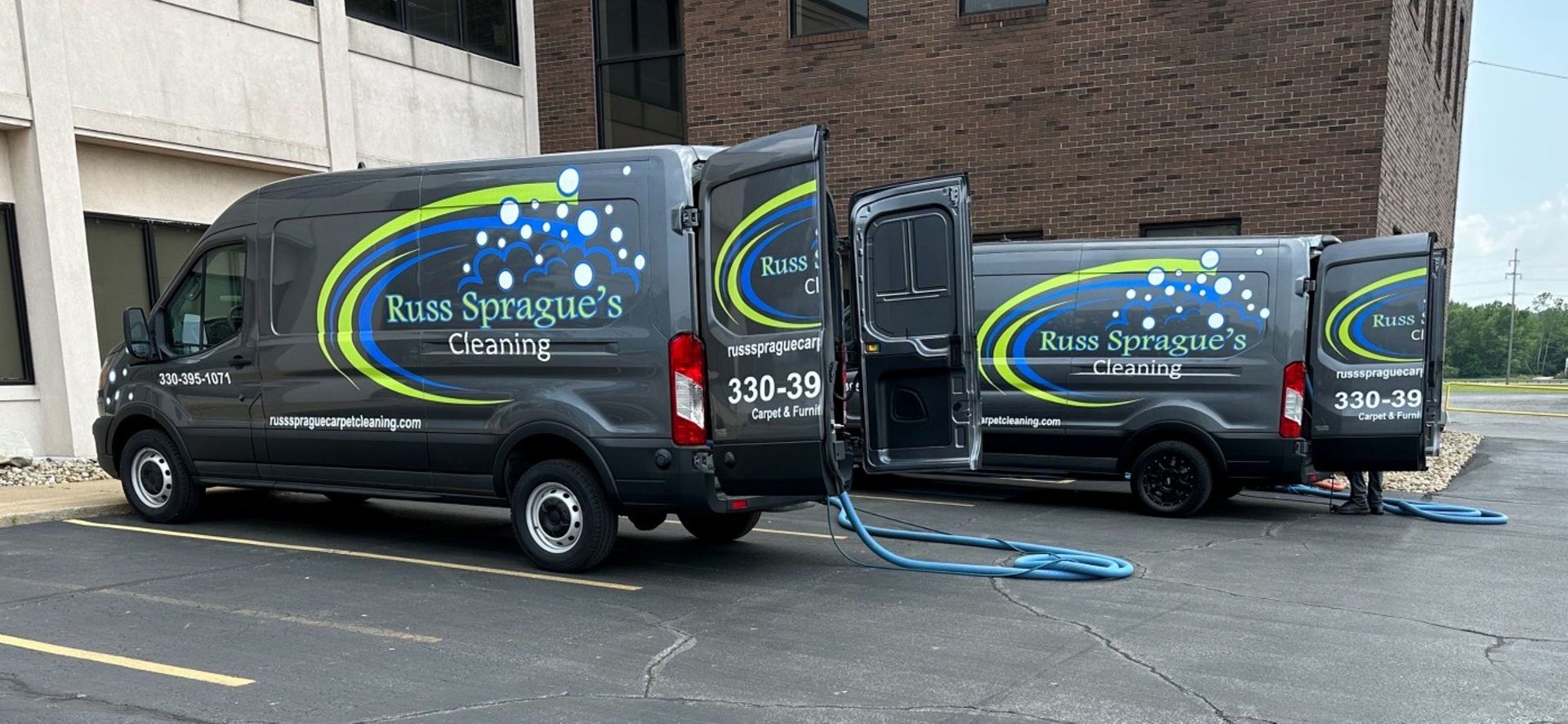 Two black company vans parked by a brick building, one with blue hoses extended across the pavement.