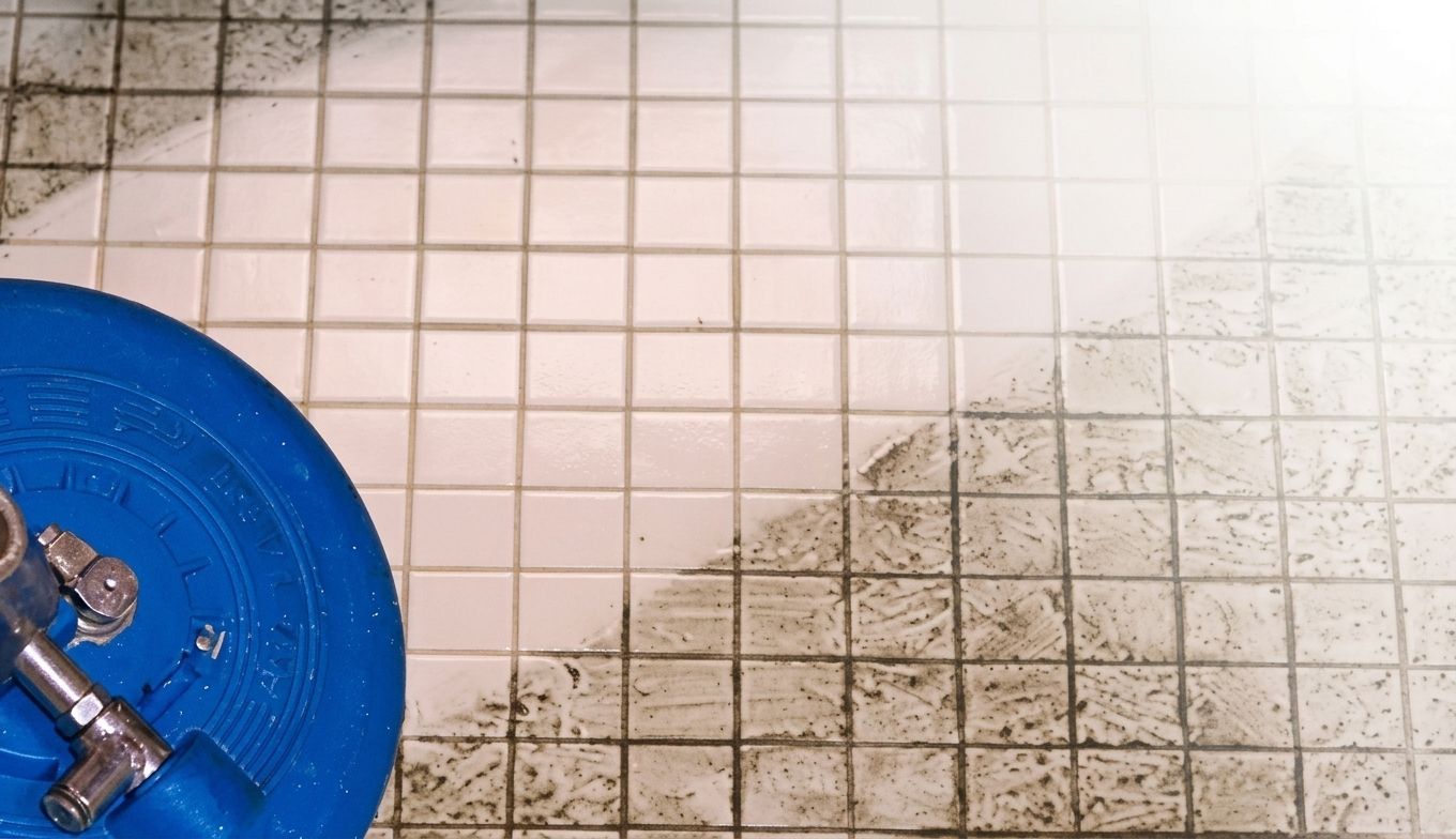 Dirty tiled floor with a blue bucket and metal fittings in the lower left corner