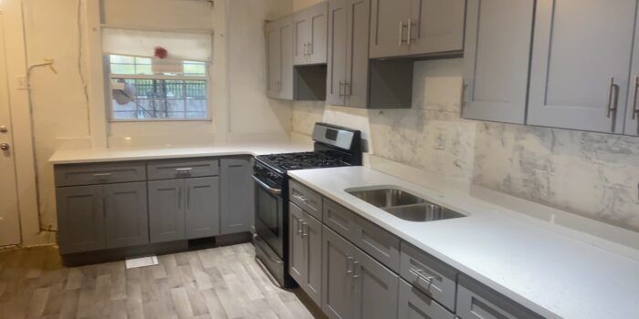 Gray kitchen cabinets with white countertops and a stainless steel stove and sink.