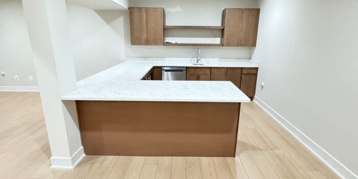 Modern kitchenette with brown cabinets, white countertops, and light wood flooring.