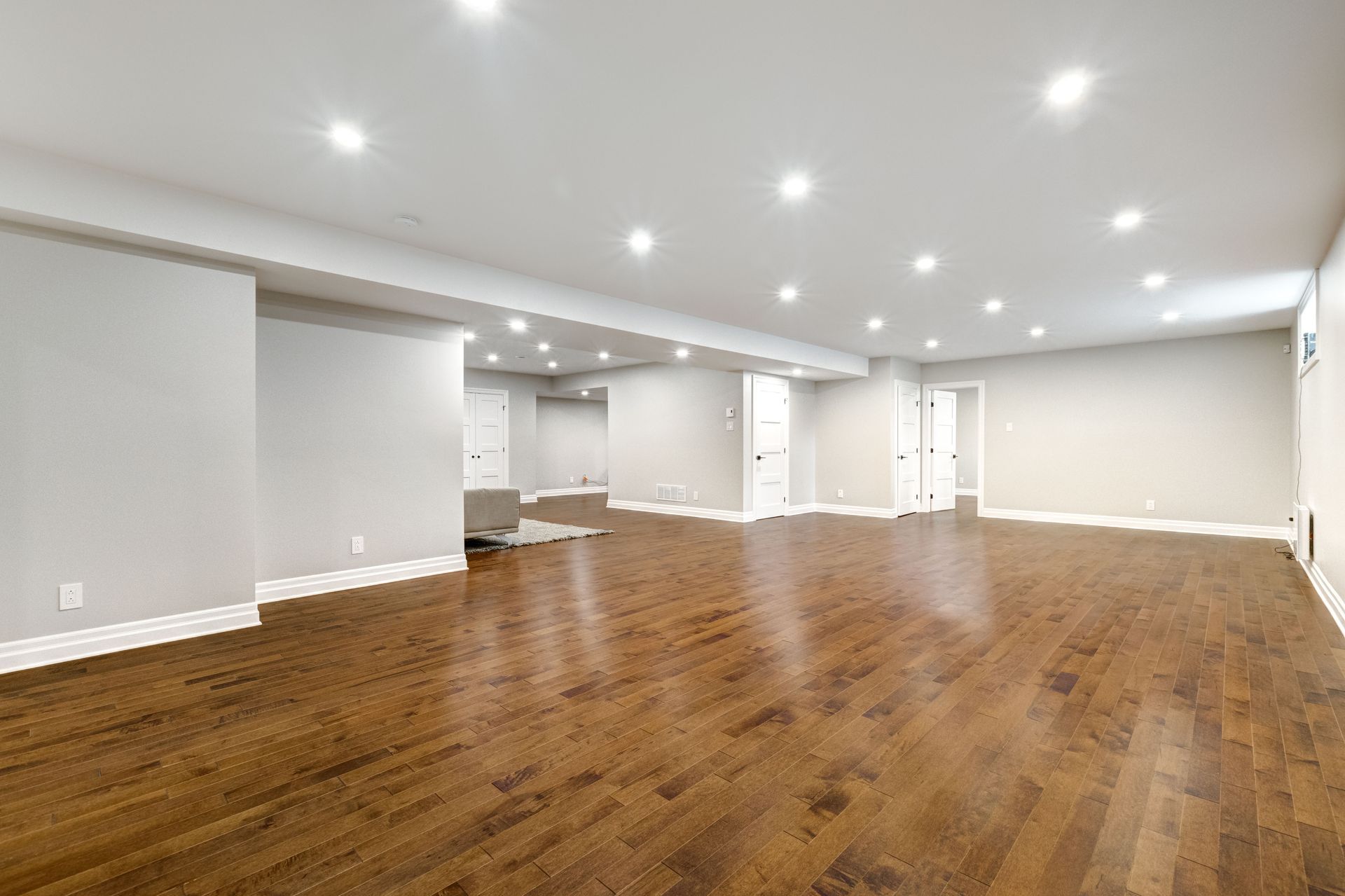 Empty, spacious room with hardwood floors, white walls, and recessed lighting.