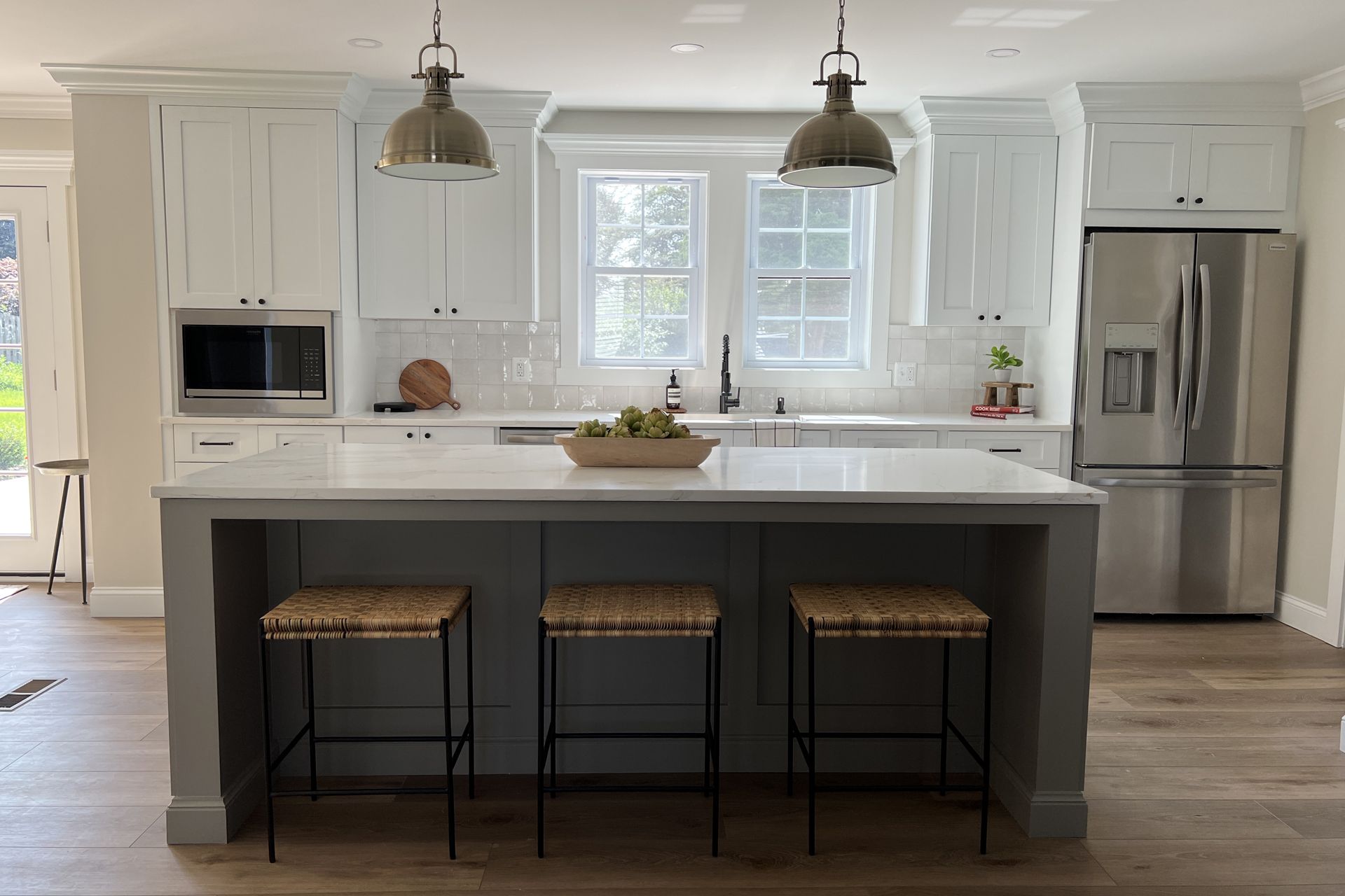 Kitchen with gray island and white cabinets, stools, stainless steel appliances.