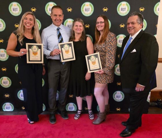 Group of people holding framed awards on a red carpet with a branded backdrop.