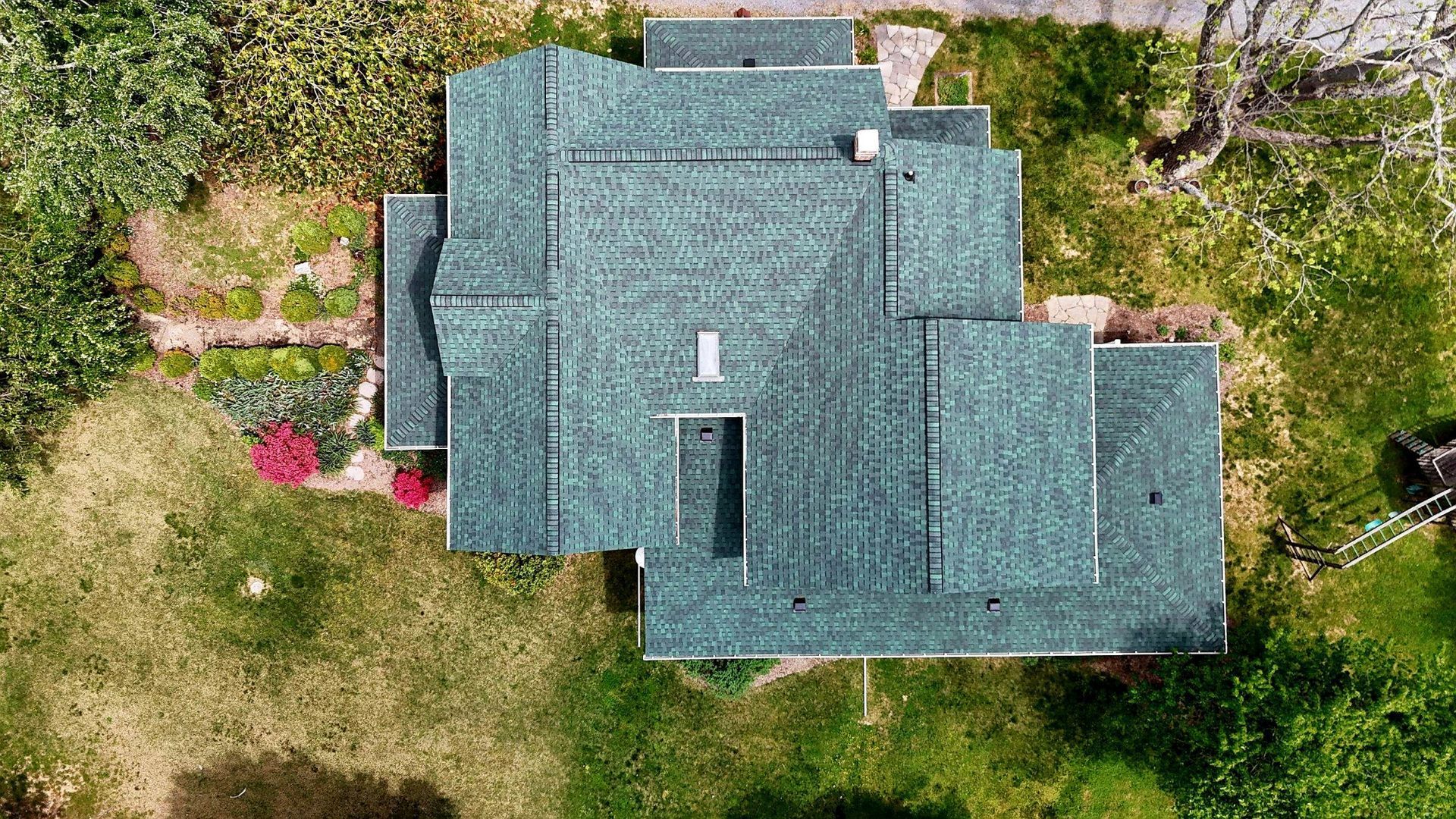 An aerial view of a house with a green roof surrounded by grass and trees.