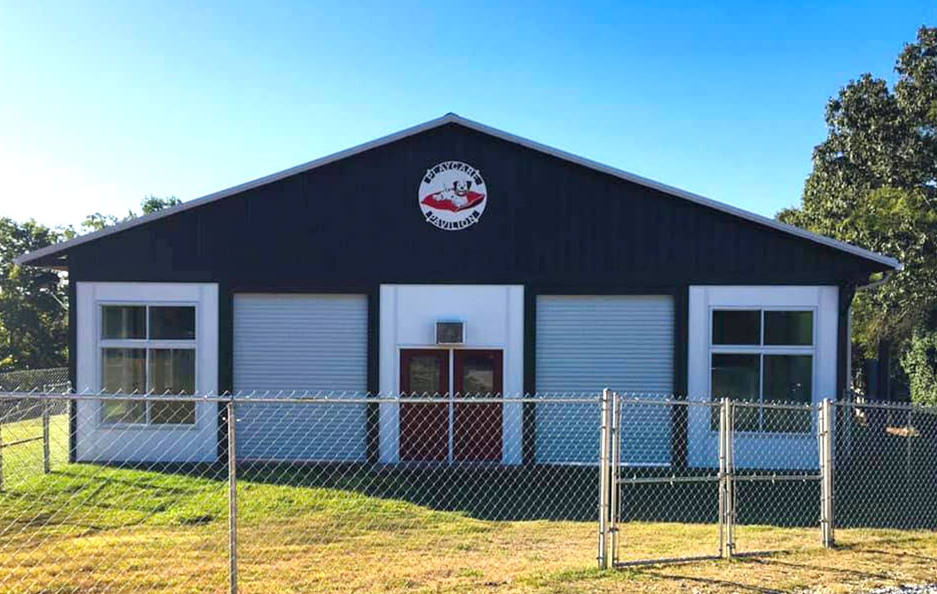 A black and white building with a red door is behind a chain link fence.