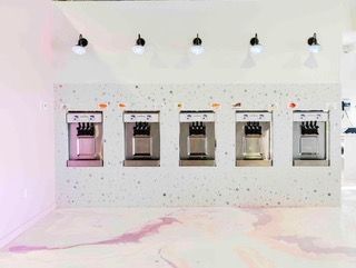 A row of soft serve machines are lined up against a white wall.