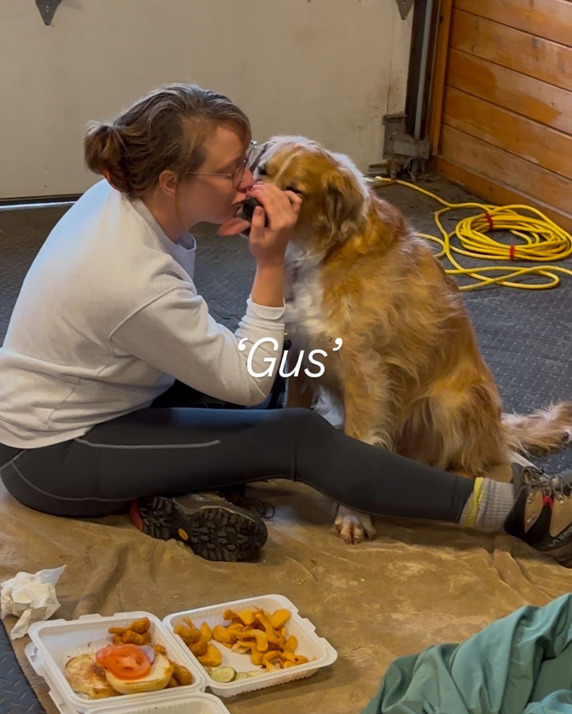 Woman kissing a golden retriever named Gus in a garage setting with food nearby.