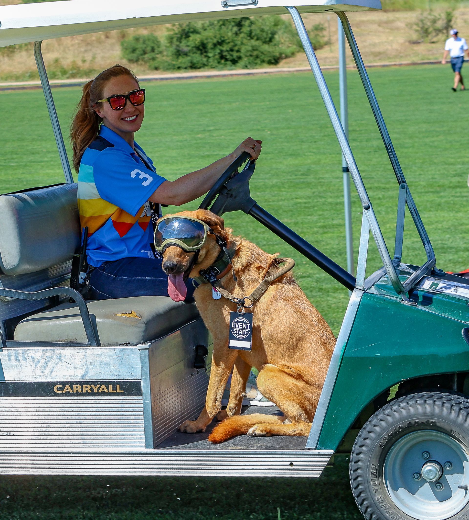 Woman and dog in golf cart on course. Dog wearing goggles.