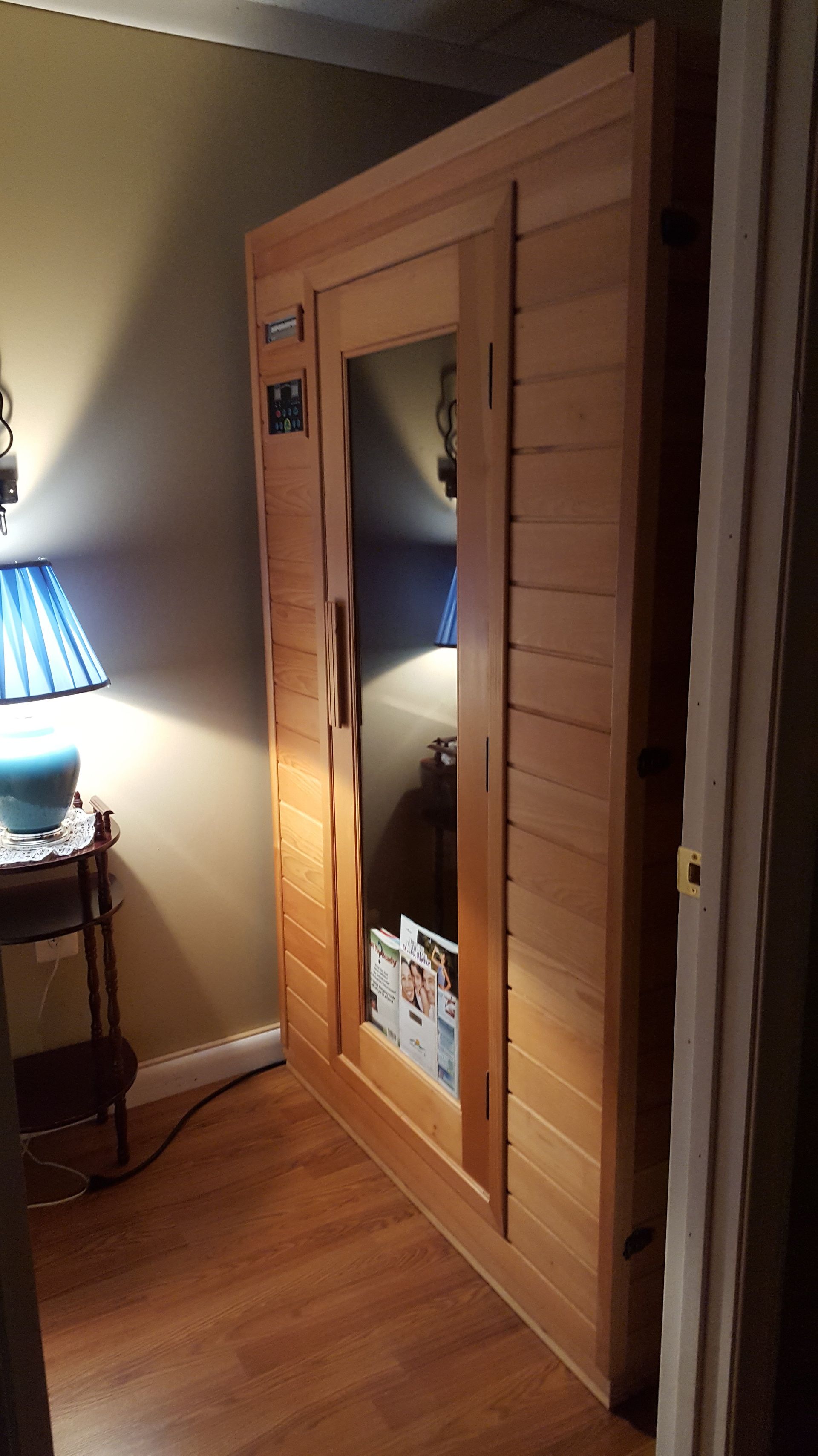 A wooden sauna is sitting in a room next to a lamp.
