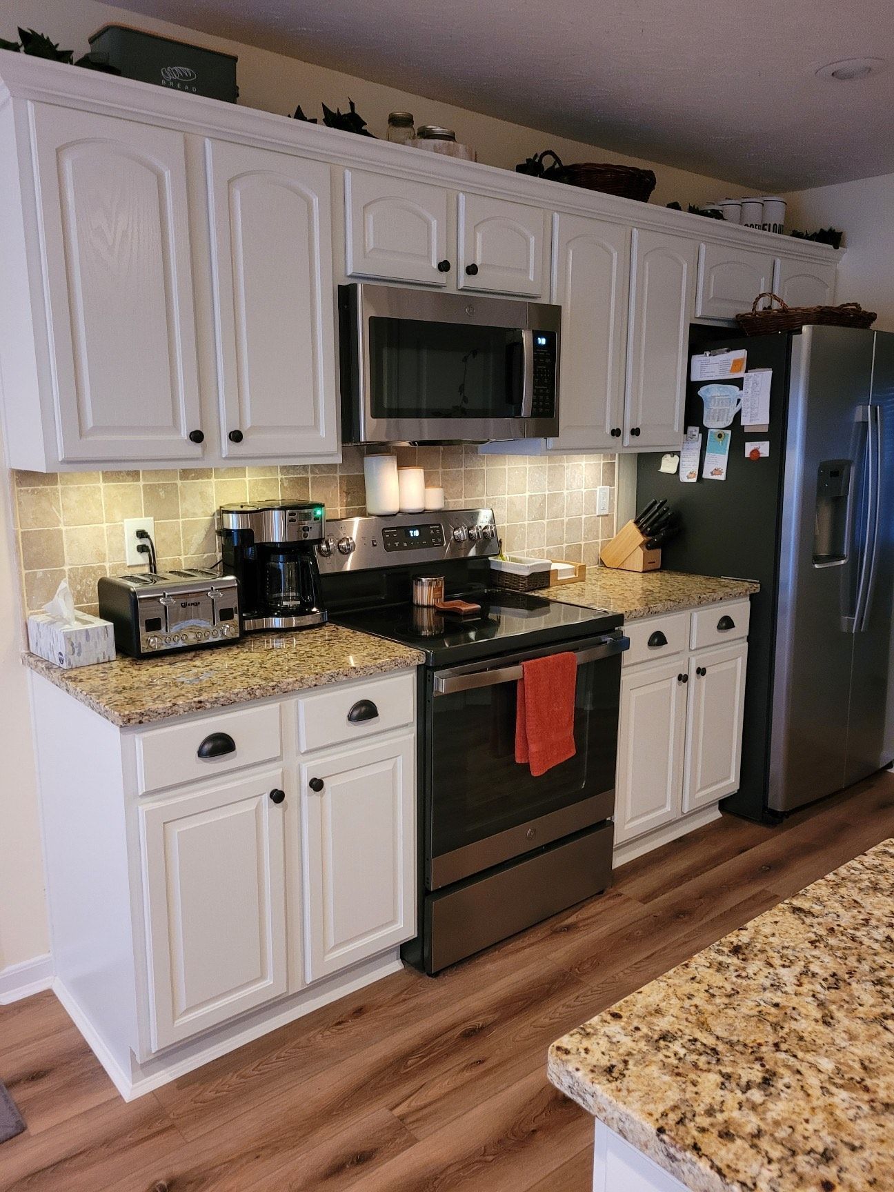 A kitchen with white cabinets , stainless steel appliances , granite counter tops and a refrigerator.