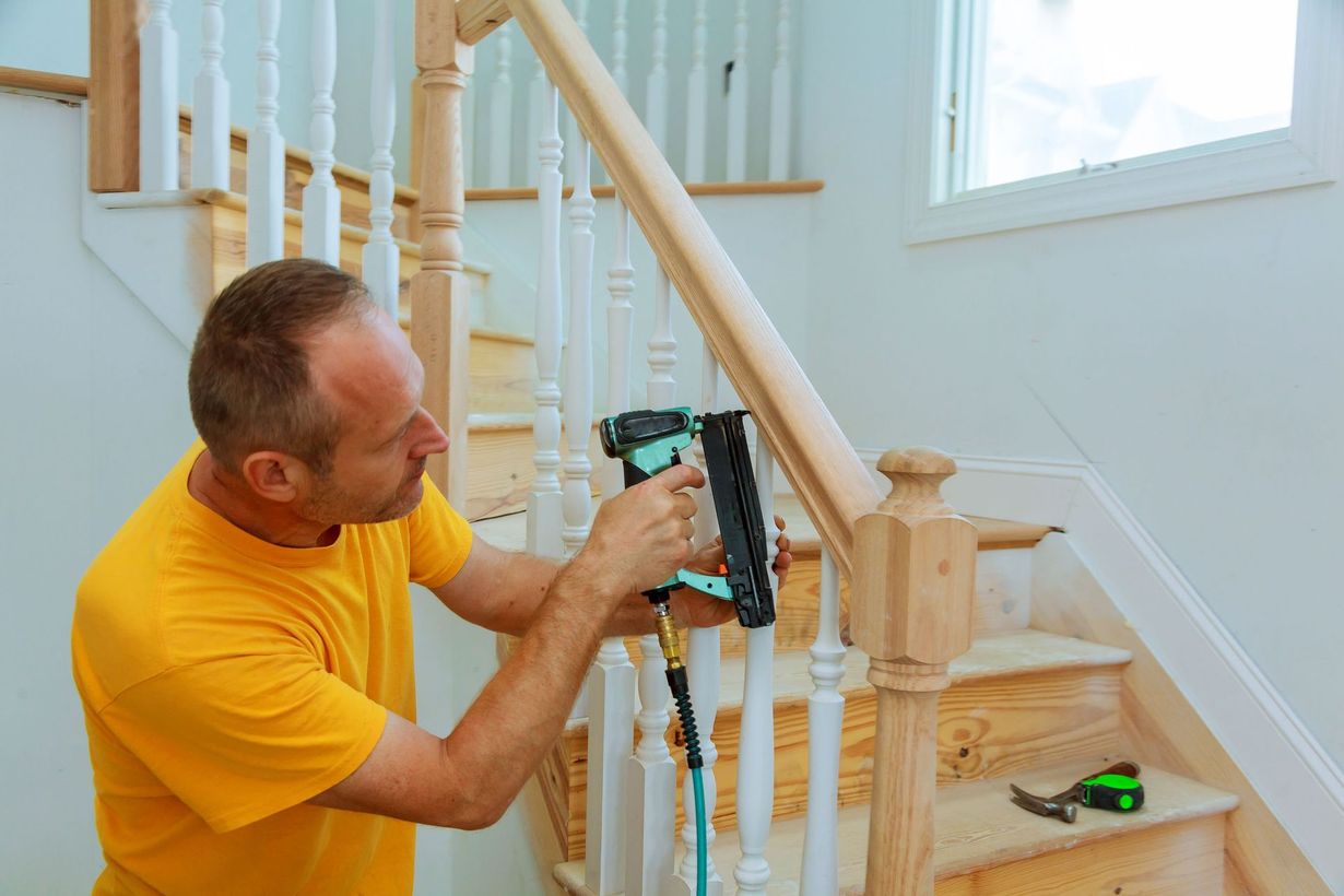 Man installing a stair railing bracket with a power drill on a wooden staircase