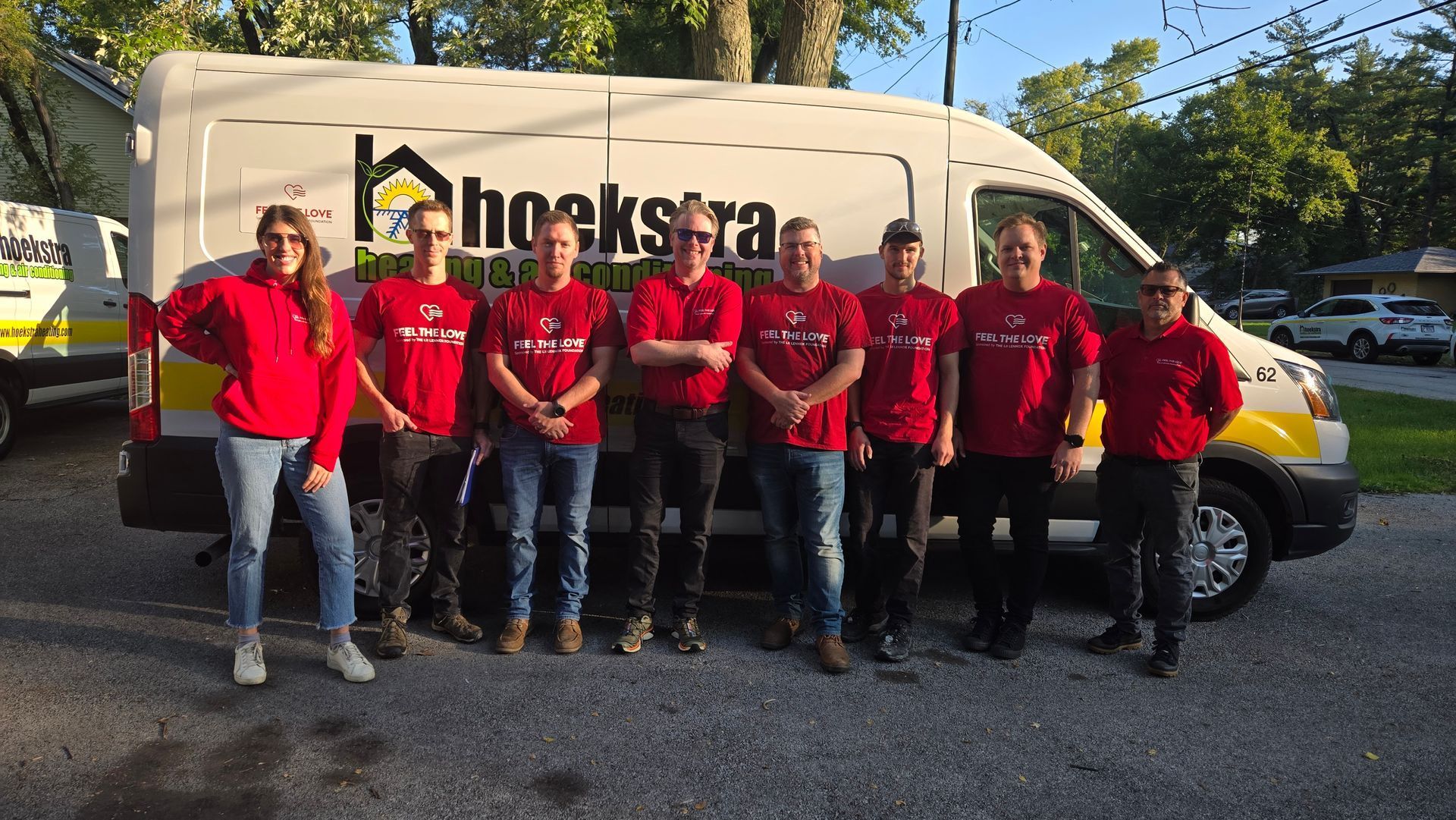 Eight people in red shirts stand in front of a white and yellow service van with a logo.