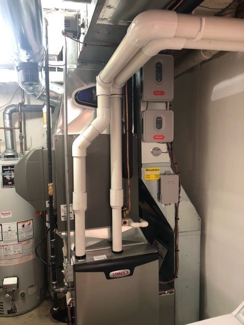Furnace and water heater in a utility room with white pipes and three gray boxes mounted on the furnace.